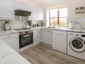 una cucina bianca con armadi bianchi e lavastoviglie di Seaview Cottage a Holt