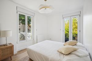 een witte slaapkamer met een bed en 2 ramen bij Maison moderne parisienne in Colombes