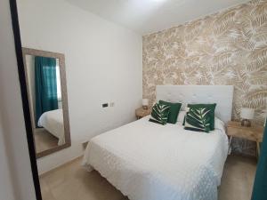 a bedroom with a white bed with green pillows and a mirror at Apartamento Faro de Sardina in Gáldar