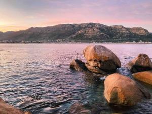 a large rock in the water with mountains in the background at The Sugarbush in Cape Town