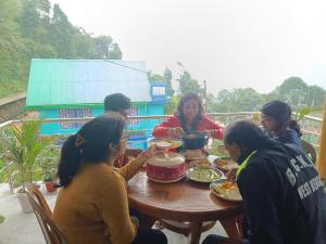 een groep mensen die rond een tafel eten bij Mountain View Passaddhi Comfort Stay in Kalimpong