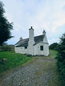 an old white house sitting on top of a field at South Lochs Cottage in Marvig