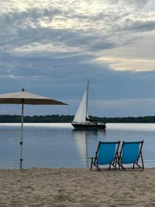 two chairs and an umbrella on a beach with a sail boat at Leipzig-Südwest in Leipzig