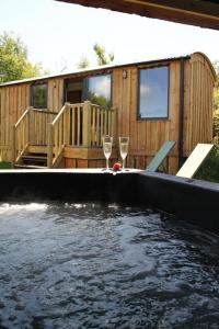a pool of water with two wine glasses in front of a house at Pembrokeshire Shepherd hut with hottub in Jordanston