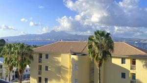 a yellow building with palm trees in the foreground at Les Ecrins, Anse Mitan, très beau F2, vue mer, proche plage in Les Trois-Îlets