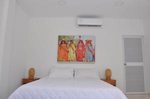 a bedroom with a white bed with a painting on the wall at AKUAIPPA HOSTAL RESTAURANT in Santa Marta