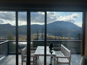 un gato sentado en un banco en un balcón con montañas en Astonishing Mountain Lodge at the top of Gaustablikk, 25m2 west facing terrace, 3 bedrooms, en Gaustablikk