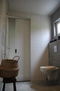 - une salle de bains pourvue de toilettes et d'un panier sur un tabouret dans l'établissement Bed & Breakfast Bij de Wilg, à Laren