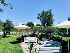 eine Terrasse mit weißen Tischen und Sonnenschirmen im Gras in der Unterkunft Olive Garden Studios & Apartments in Acharavi