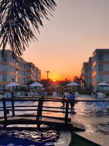 Sonnenuntergang über einem Park mit einer Bank und Gebäuden in der Unterkunft Maraújosflat, Porto de Galinhas in Porto De Galinhas