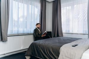 a man reading a book in front of a bed at Atomihotel: Contemporary Comfort Steps from the Atomium! in Brussels