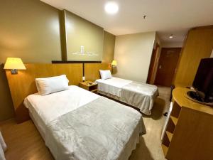a hotel room with two beds and a television at Flat 213 - Comfort Hotel Taguatinga in Taguatinga