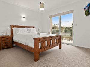sypialnia z drewnianym łóżkiem i dużym oknem w obiekcie Snoqualmie 3 2 Cobbodah St w mieście Jindabyne