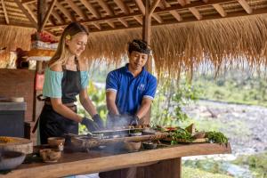 mężczyzna i kobieta gotują jedzenie na grillu w obiekcie Natya River Sidemen w mieście Silebeng