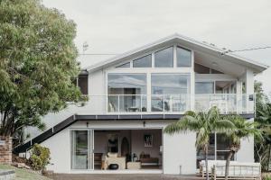 een wit huis met grote glazen ramen bij Baybreeze 18 Tomaree Road WiFi Air Conditioning Kitchenette in Shoal Bay