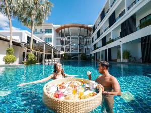 a man and woman in a swimming pool with a basket of food at The Pago Design Hotel Phuket-SHA Plus in Phuket