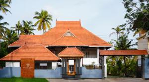 an orange roofed house with palm trees in the background at Kalloos Island Backwater Resort in Kollam