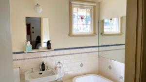 een badkamer met een bad, een wastafel en een spiegel bij Kelly House in Beechworth