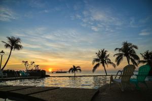 uma piscina com palmeiras e o oceano ao pôr do sol em EHSAN SEAVIEW HOTEL PORT DICKSON em Porto Dickson