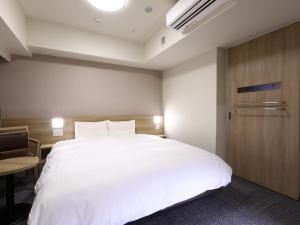 a bedroom with a white bed and a wooden door at Dormy Inn Hiroshima Annex in Hiroshima