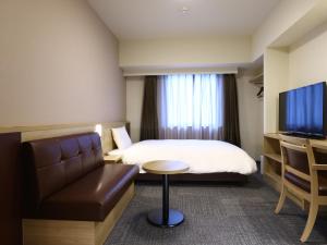 Dormy Inn Hiroshima Annex في هيروشيما: غرفه فندقيه بسرير واريكه