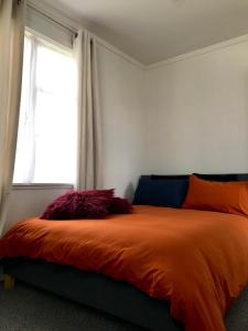a bedroom with a bed with an orange comforter and a window at Santos Place in Auckland