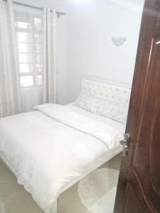 a bedroom with a bed with white sheets and a window at Carlyle comfort home in Thika