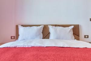 a bed with two white pillows and a red blanket at Deluxe by Alz in Mamaia Sat/Năvodari