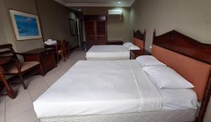 two beds in a hotel room with a desk and a table at Hotel Ming Kiong in Rumah Chaong