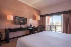 a hotel room with a bed and a desk and a window at Vila Gale Collection Praia in Albufeira