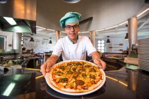 a chef holding a large pizza in a kitchen at Vila Gale Collection Praia in Albufeira