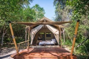 a tent in the woods with a bed in it at Cha Cha Metsi in Maun