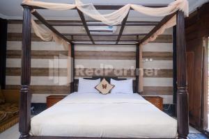 1 dormitorio con cama con dosel, sábanas y almohadas blancas en Kebon Krapyak Cottage Syariah Mitra RedDoorz near Stadion Maguwoharjo, en Yogyakarta