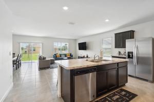 a kitchen with a stainless steel refrigerator and a living room at Brand New 4-Bedroom House near Disney & Beaches! in Port Saint Lucie