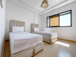 two beds in a white room with a window at La Perle Taghazout apparts 2-3px in Taghazout
