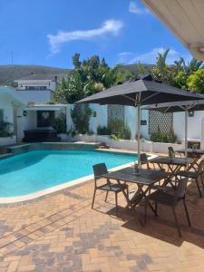 ein Pool mit zwei Tischen und einem Sonnenschirm in der Unterkunft Thyme Wellness Spa and Guesthouse in Kapstadt