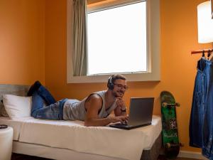 un hombre acostado en una cama con un portátil en ibis budget Sao Paulo Paraiso, en São Paulo