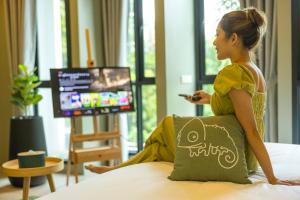 una donna seduta su un letto con un telecomando di Chamemon Bed Phuket Town a Phuket