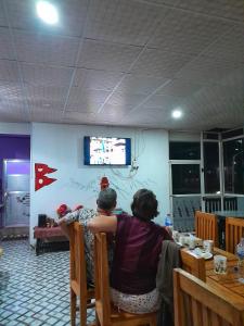 two people sitting at a table watching a television at Himchuli Guest House in Bandipur