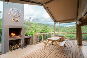 a fireplace on a deck with a bench and a table at AfriCamps Addo in Swanepoelskraal