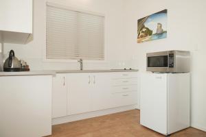 a white kitchen with a microwave and a refrigerator at Beachfront Resort in Whitianga