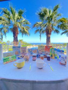 a table with cups and spoons and palm trees at Rais Gerbi Appartamento in Pollina