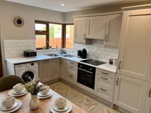 eine Küche mit weißen Schränken und einem Tisch mit Geschirr in der Unterkunft Sarah’s cottage in Newry