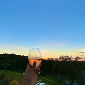 a person holding a glass of wine at sunset at Espaço Vento Solar in São Roque