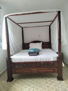 a bed with a wooden canopy bed with a pillow on it at Diani Hideaway Beach Villa in Galu