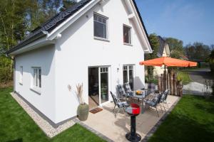 Cette maison blanche dispose d'une terrasse et d'un parasol orange. dans l'établissement Ferienhaus Sturmmöwe Zingst, à Zingst