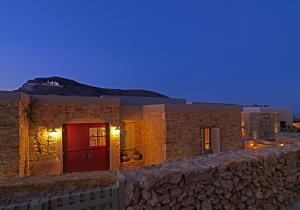 una casa con una puerta roja y una pared de piedra en Themonies Luxury Suites, en Chora Folegandros
