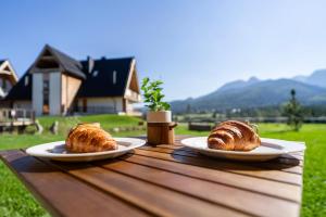 two croissants sitting on plates on a wooden table at Apartamenty Zana by Apart Concept Podhale in Kościelisko