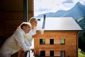 a man and woman holding a cup of coffee on a balcony at Alpenstolz Damüls Haus 2 - Stilvoll urlauben in den Bergen in Damuls