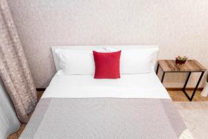 uma cama branca com uma almofada vermelha em Яркая Квартира на Арбате em Almaty